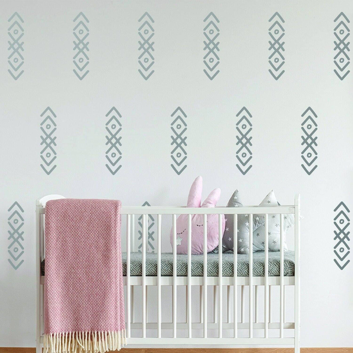 WhimsyArrows vinyl wall decals in nursery with crib, colorful plush toys, and pink throw blanket for whimsical decor.