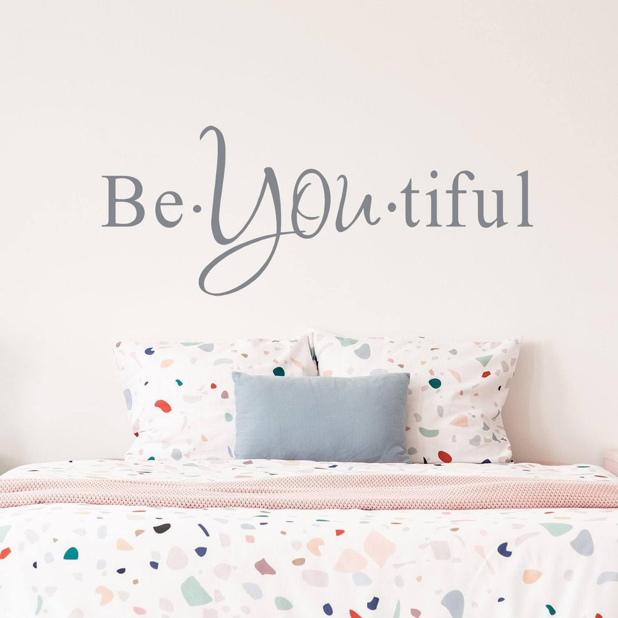 Motivational wall decal "Be YOU tiful" above a colorful polka dot bedspread, adding charm to any room.