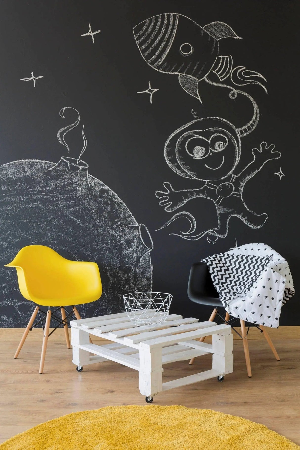 Creative chalkboard wall art featuring a rocket and astronaut in a stylish living space with yellow and black chairs.