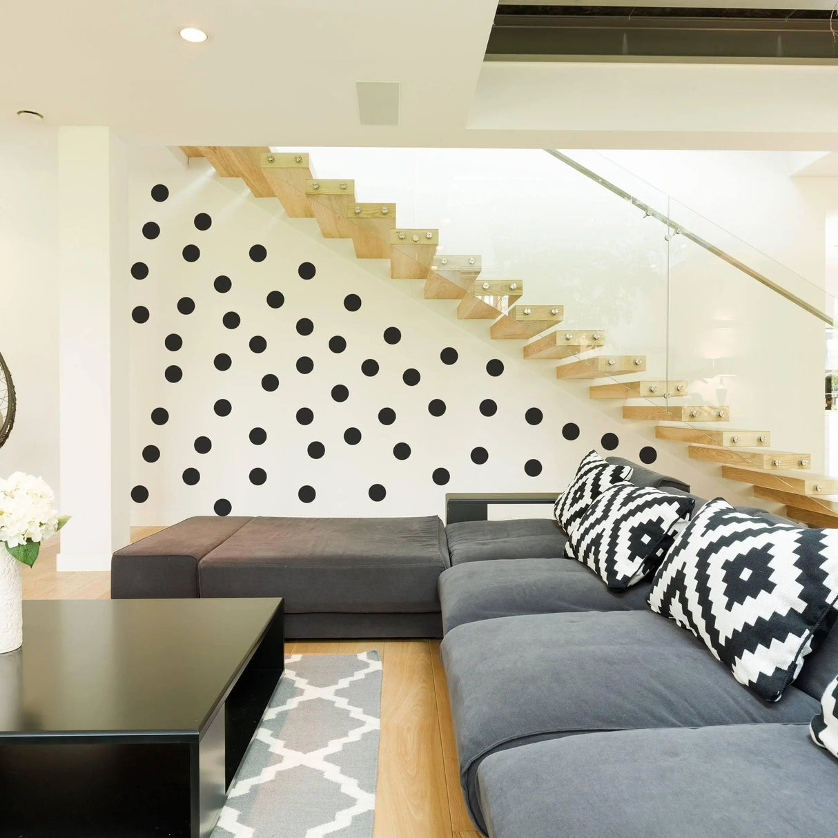 Modern living room featuring black circle wall stickers on a white wall behind a stylish gray sofa and wooden staircase.