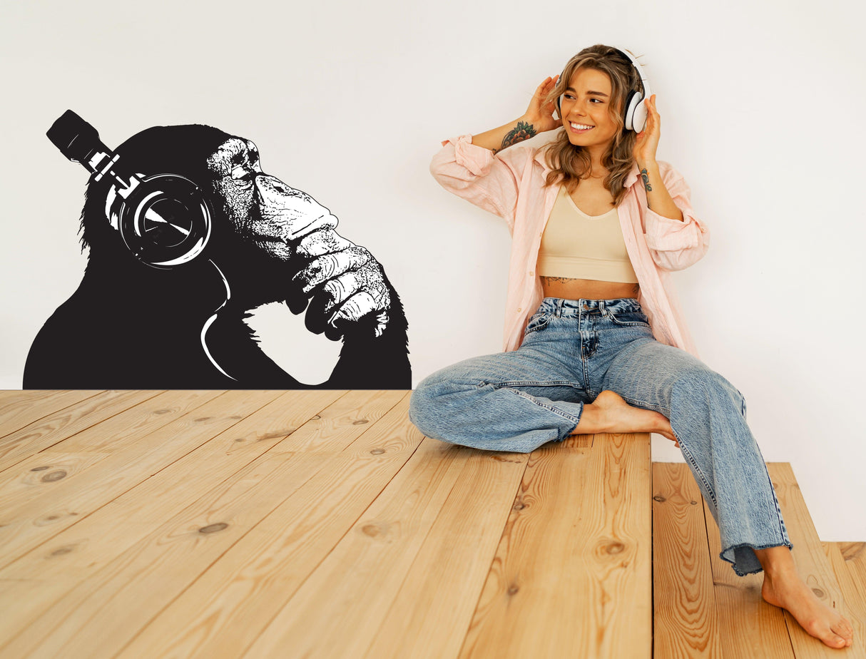 Stylish woman sitting on wooden floor with vinyl wall art of contemplative chimp wearing headphones.