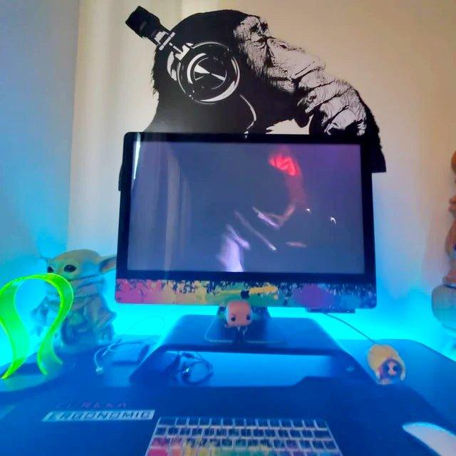 Vinyl wall art decal of a contemplative chimp wearing headphones above a colorful desk setup with glowing lights.