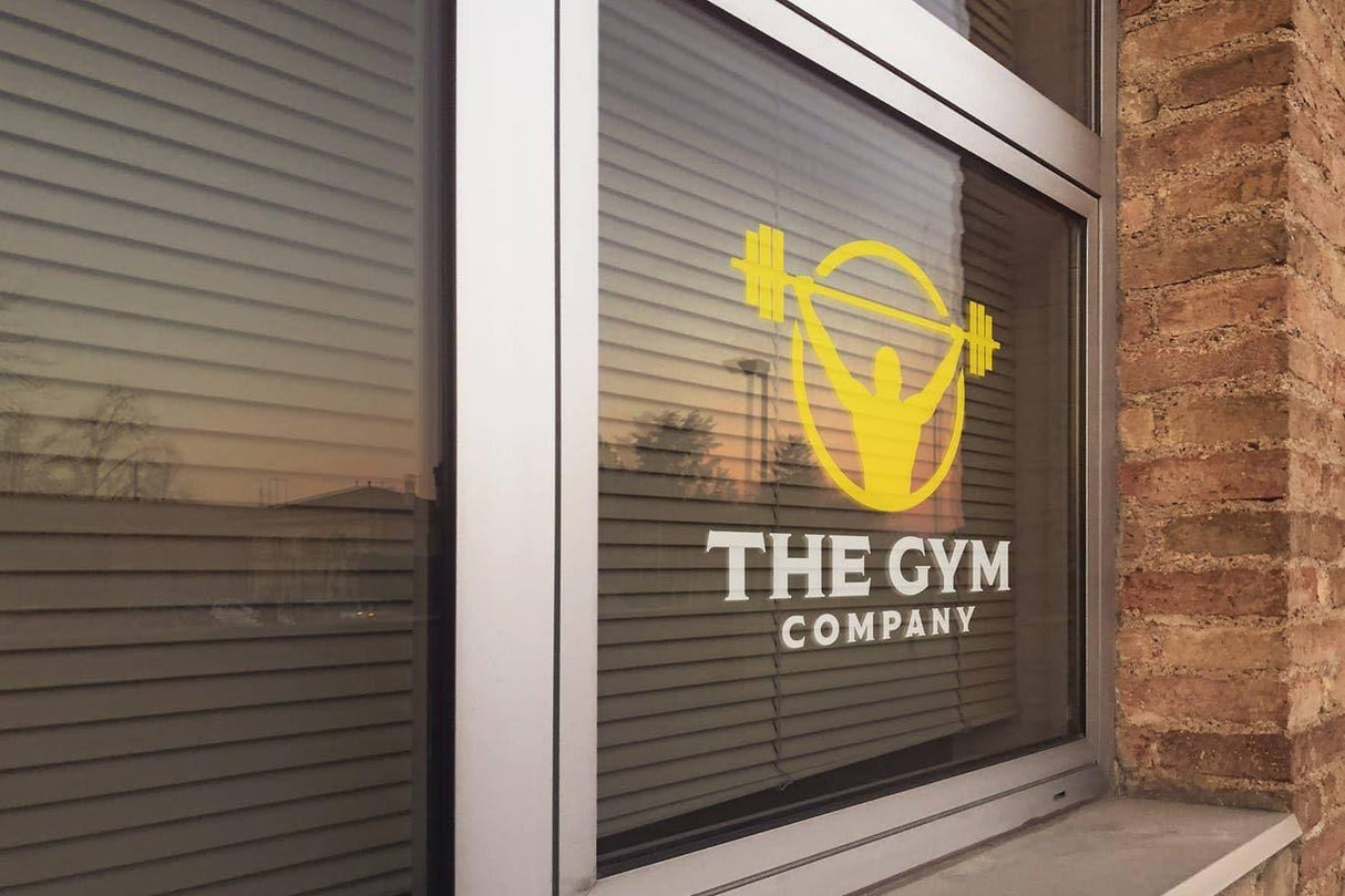 Window decal of The Gym Company logo featuring a weightlifter silhouette.