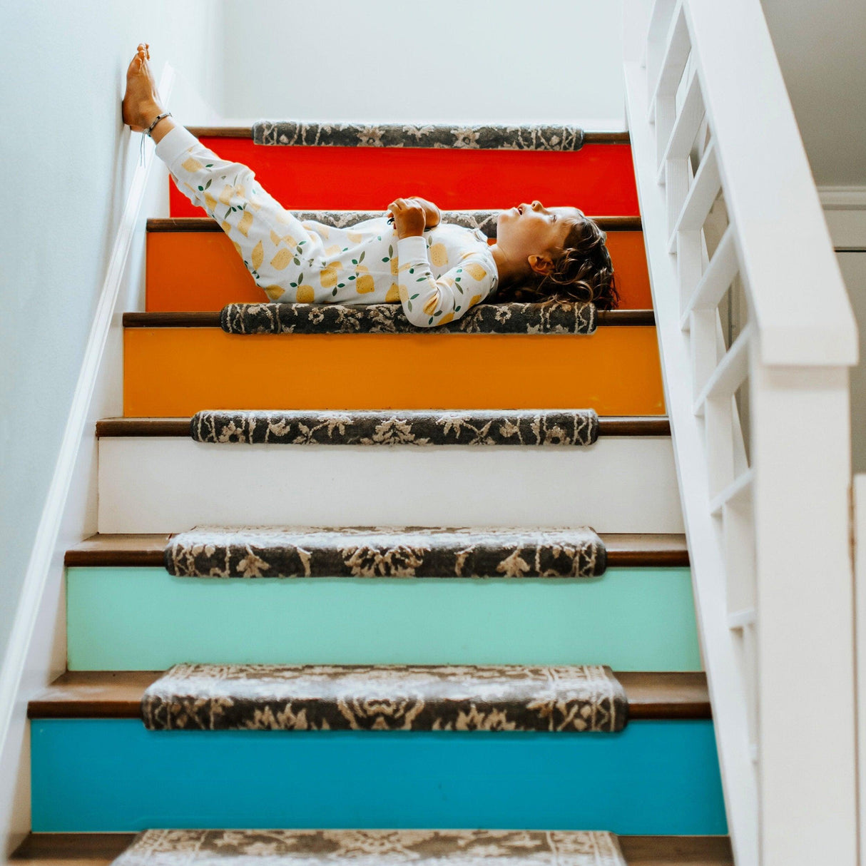 Child lounging on vibrant gradient stair risers with colorful decals, showcasing playful staircase transformation.
