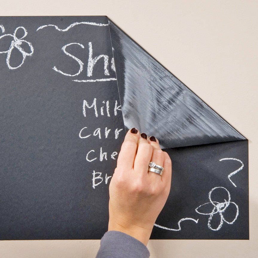 Person peeling back Large Chalkboard Wall Decal with handwritten grocery list and doodles.