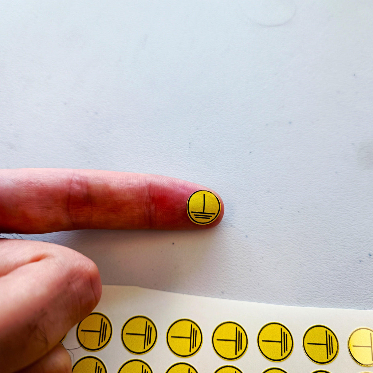 Close-up of a finger with a small yellow electrical hazard sticker, highlighting safety compliance with vinyl decals.