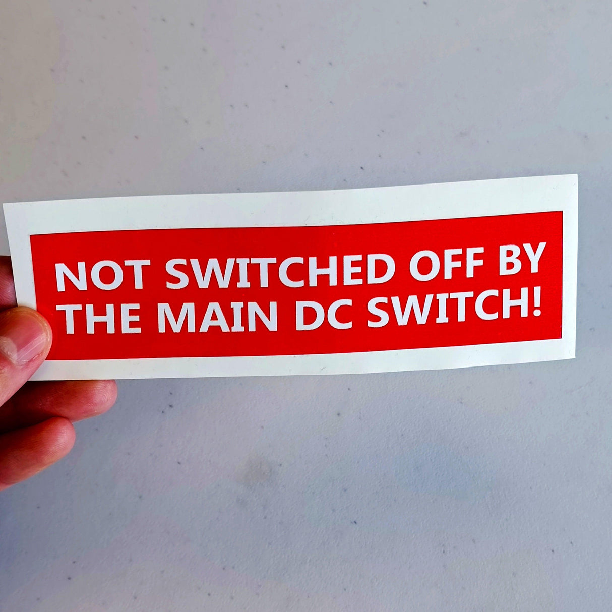 Safety label decal stating 'Not Switched Off by Main DC Switch' for electrical warning and compliance.