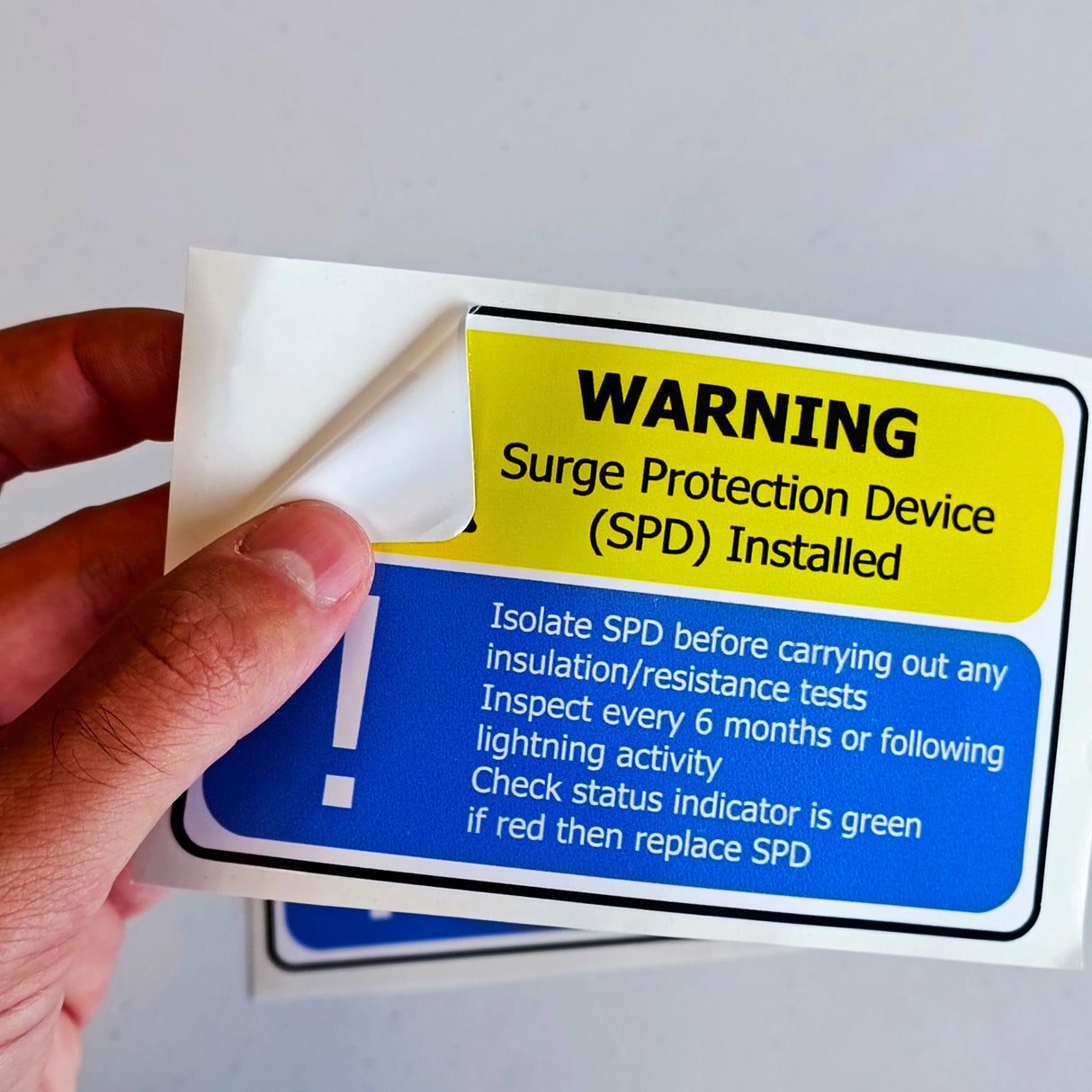 Hand holding a Surge Protection Device (SPD) warning label with clear safety instructions.