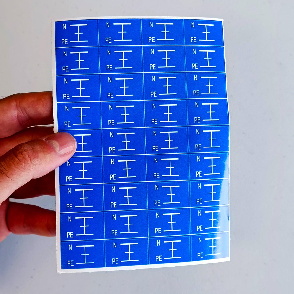 Blue electrical component labels showing Neutral (N) and Protective Earth (PE) symbols on a sticker sheet.