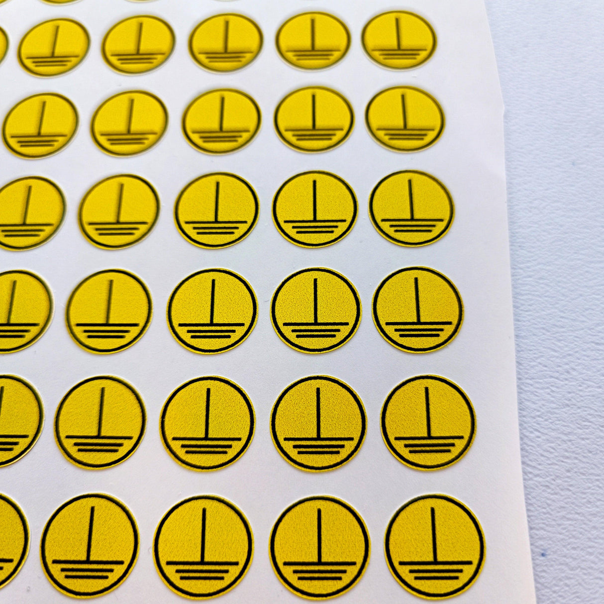 Yellow vinyl electrical safety stickers in circular design, showing grounding symbol for safety compliance.