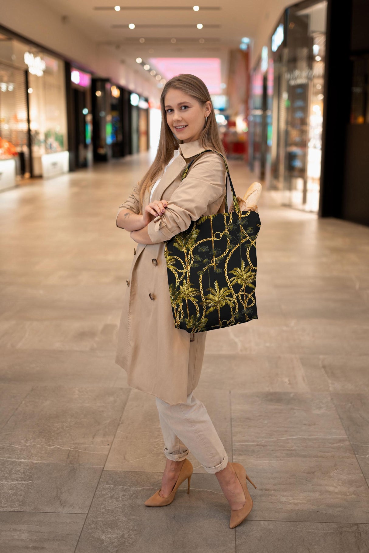 Stylish woman carrying a black tote bag with palm tree design in a modern shopping mall.