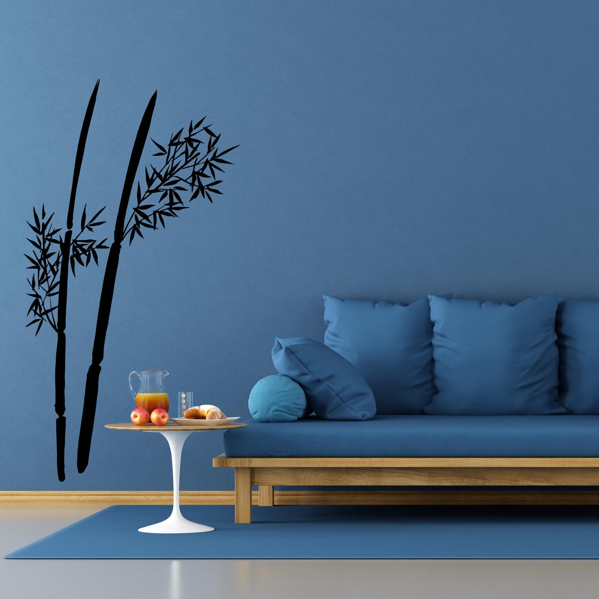 Bamboo wall decal on blue wall above a modern couch with colored pillows and a table with fruits and a pitcher.