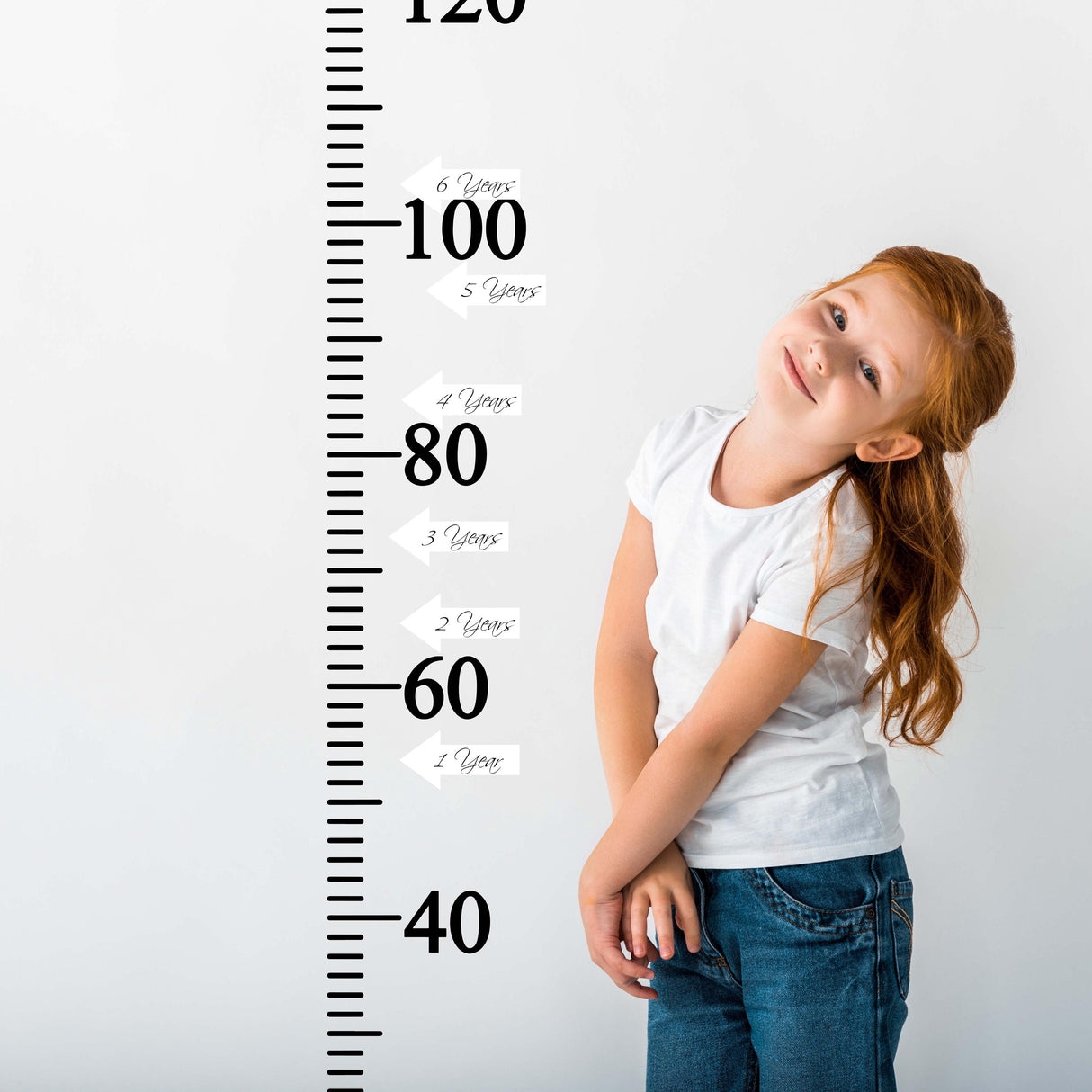 Child smiling beside a vinyl growth chart ruler with white arrow stickers marking height milestones in centimeters.