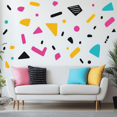 Colorful geometric Memphis pattern wall decals on a white wall above a modern couch with colorful pillows.