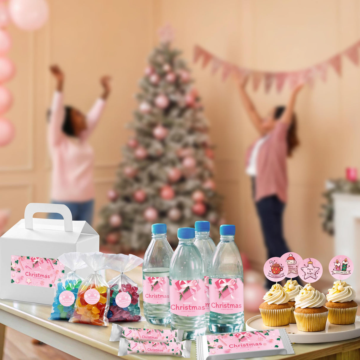 Pink Christmas sticker set displayed on bottles and gifts at a festive holiday gathering with a decorated tree.