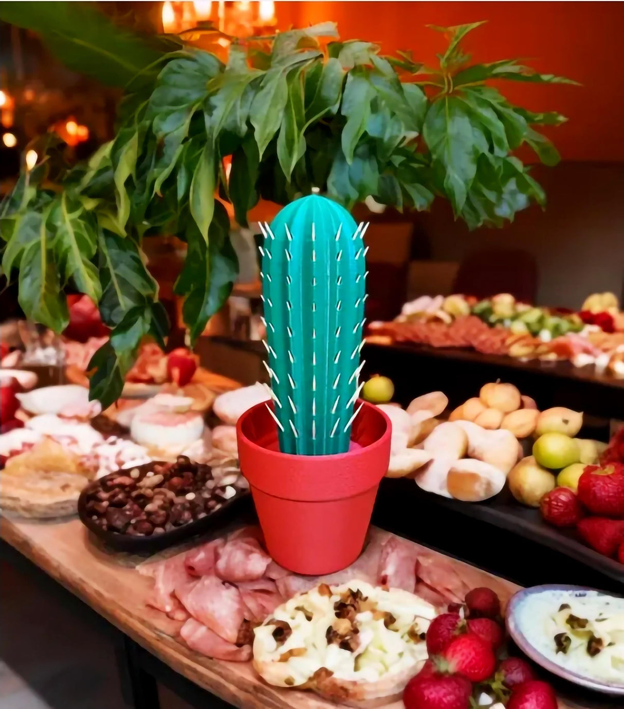 3D printed cactus toothpick holder in a red pot on a party table with cheese and fruits.