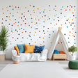 Colorful polka dot wall decals in a playful kids room with white couch and teepee, bright cushions, and greenery.