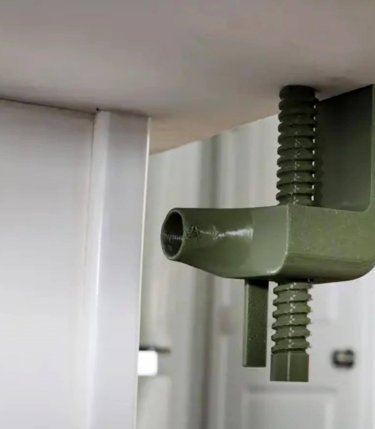 Close-up of a green clamp securely attached under a table for mounting accessories.