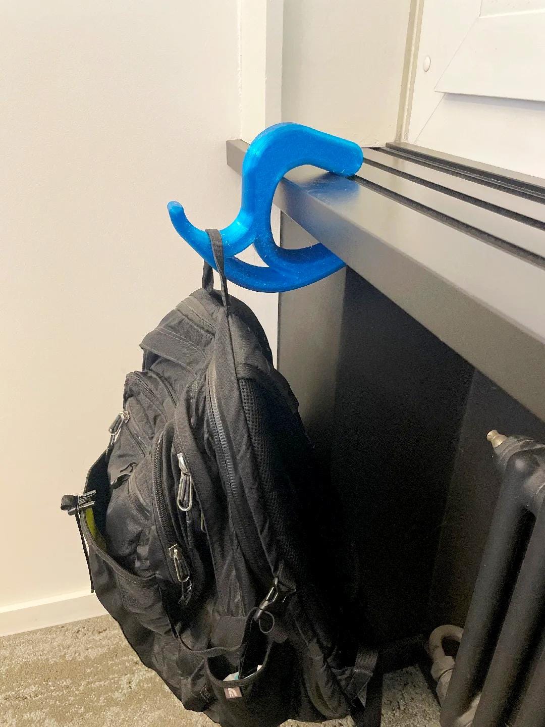 Blue 3D printed desk bag hook holding a black backpack, showcasing a universal desk accessory for keeping bags off the floor.
