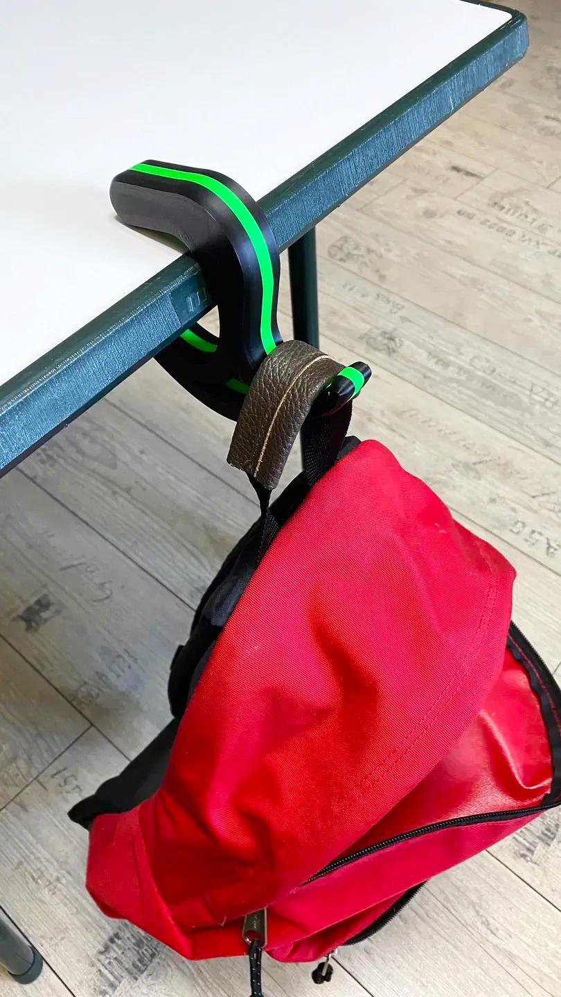 Desk bag hook holding a red backpack under a table, showcasing a portable accessory for keeping bags off the floor.