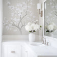 Chinoiserie tree wall decal with white flowers in a light gray bathroom, featuring a modern sink and vase of hydrangeas.