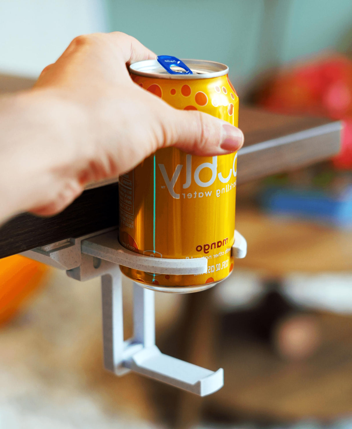 A hand holding a can of soda supported by a fold-out under desk cup holder, showcasing its minimalist design and functionality.
