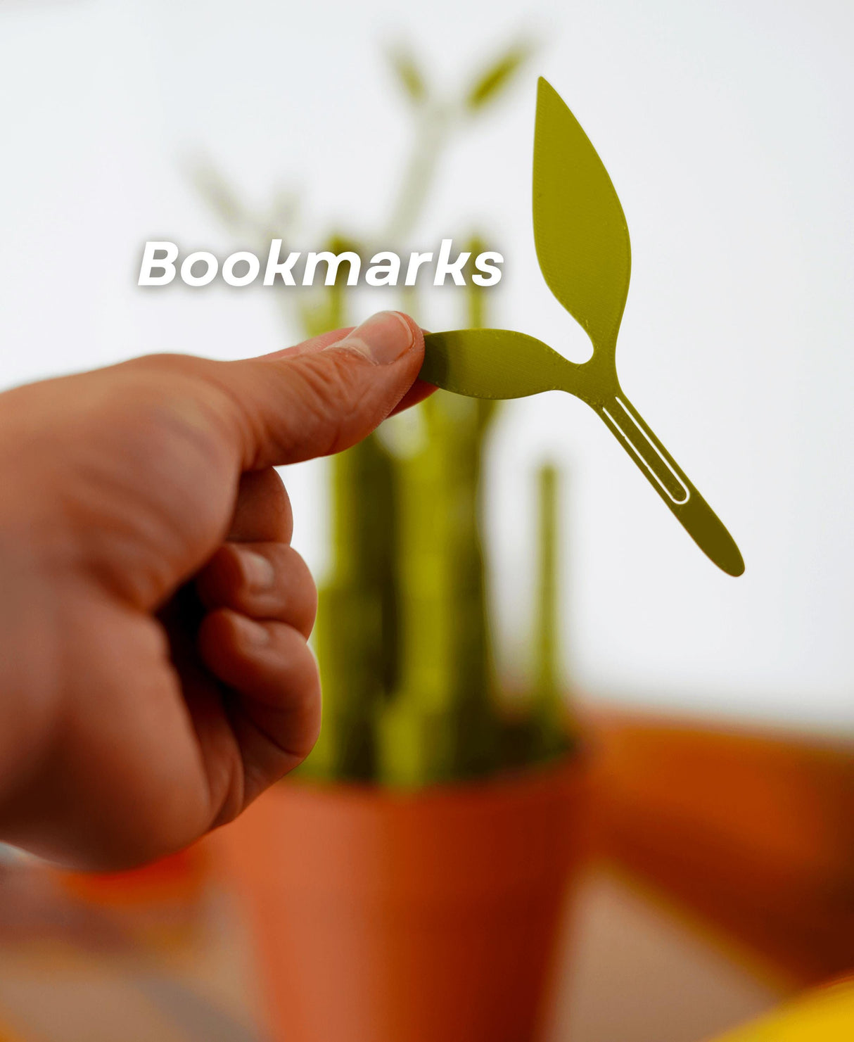 Hand holding a green leaf-shaped bookmark with a bamboo plant in the background, showcasing a stylish desk accessory.