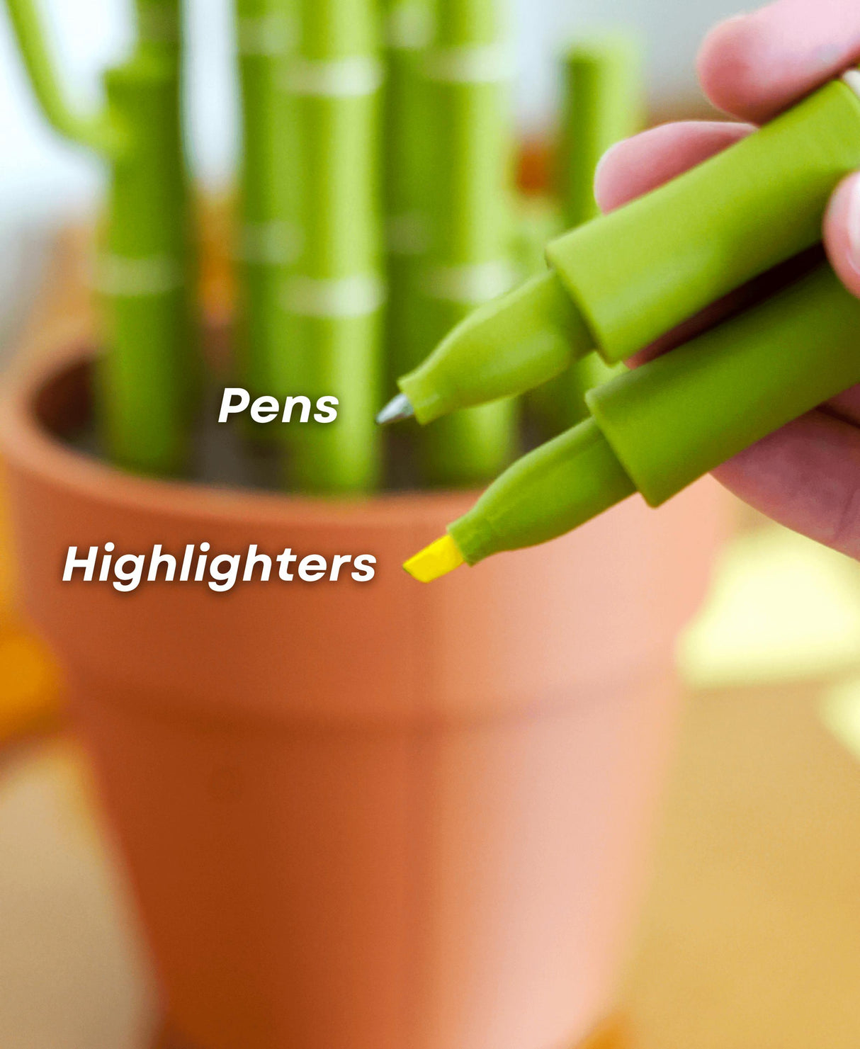 Green pens and highlighters held above a bamboo plant in a terracotta pot, perfect for desk organization.