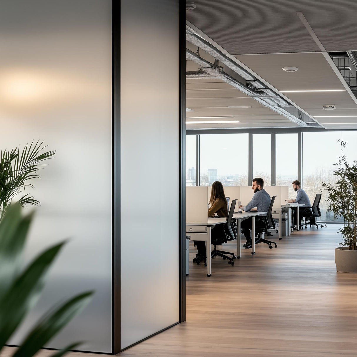 Modern office interior featuring frosted glass partitions and employees working at desks.