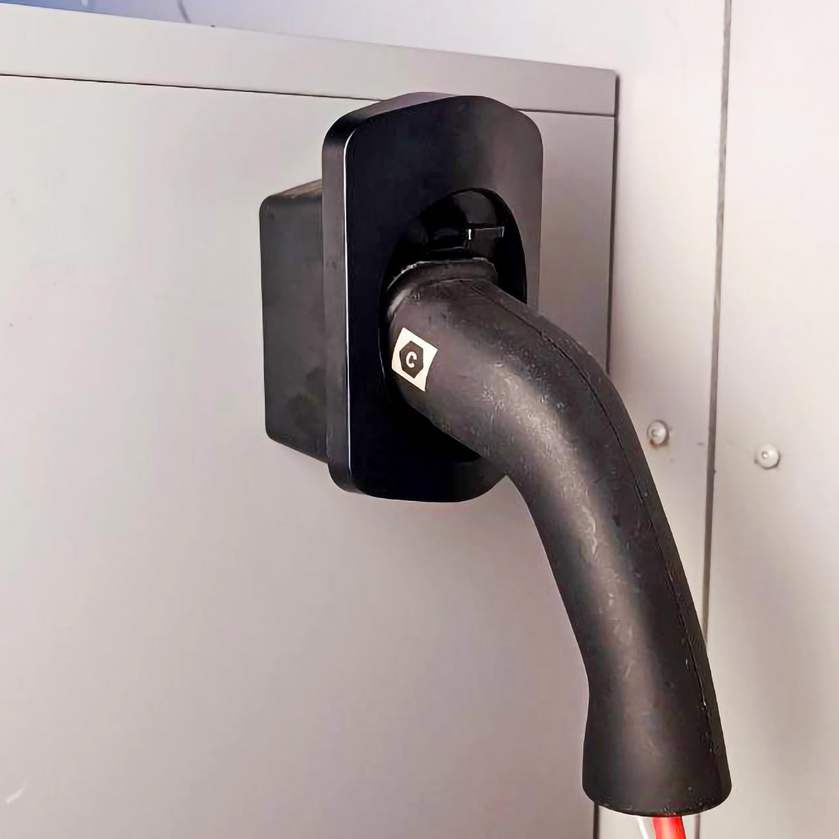 Wall-mounted electric car charger connector holder with charging cable attached.