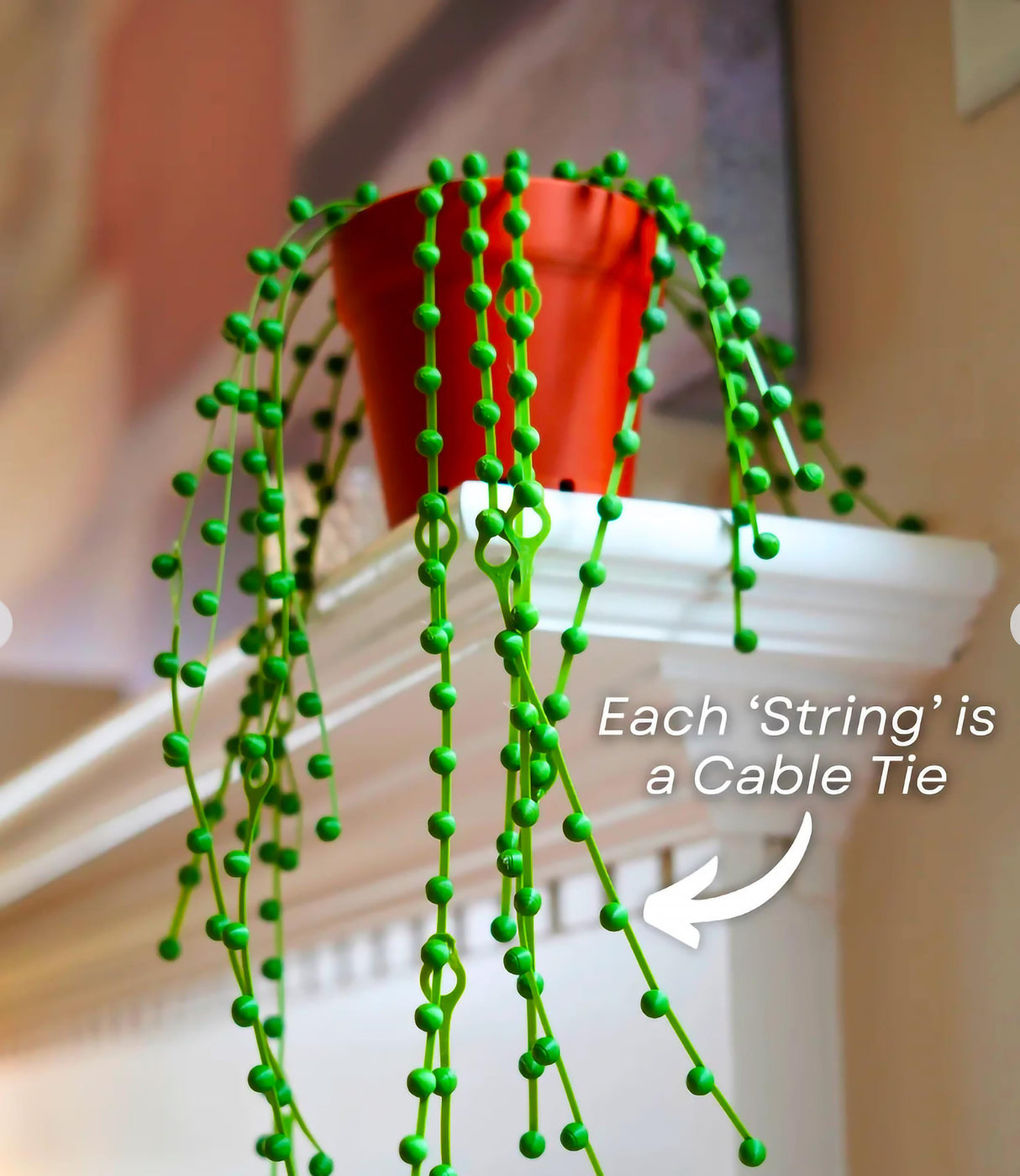 Green plant-inspired cable organizer with cascading strings as cable ties on a shelf.