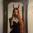 Woman in gothic attire wearing 3D printed red demon horns in front of a mirror, showcasing a striking cosplay look.
