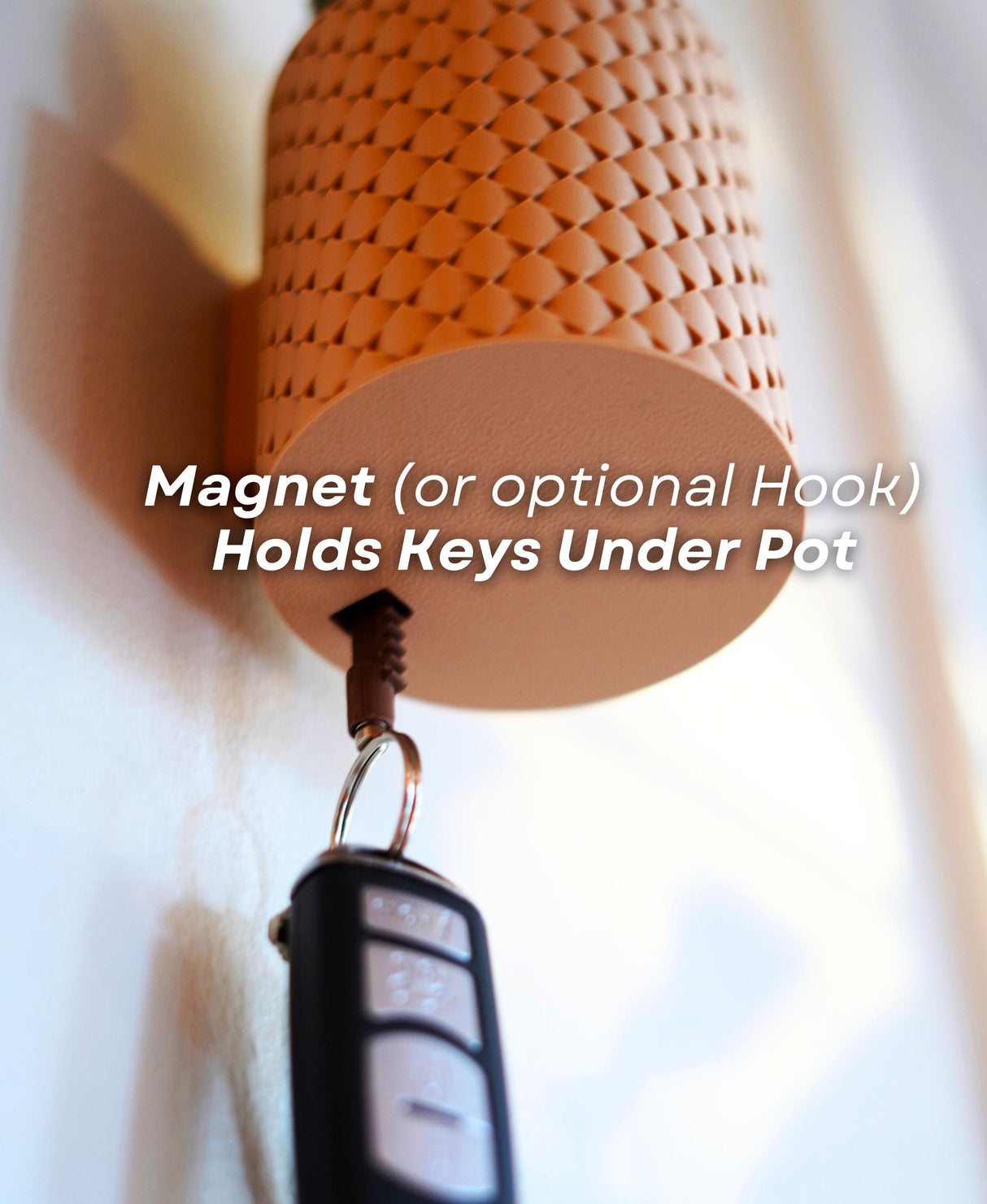 Close-up of a magnet or hook key holder under a pot, showing keys attached for convenient storage.
