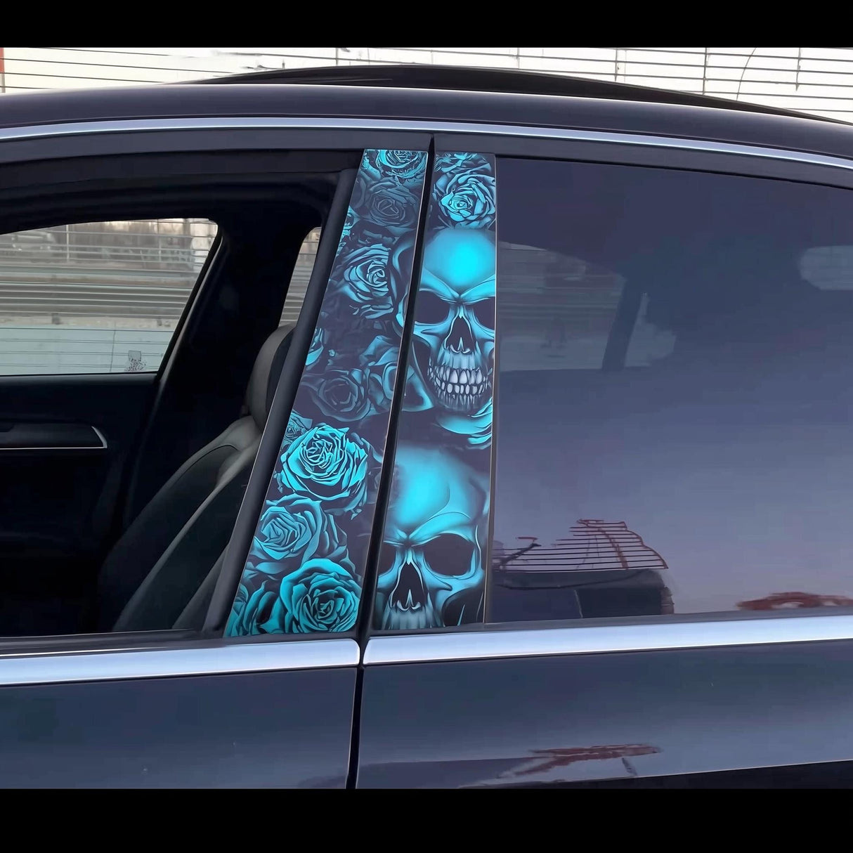 A close-up of a black car featuring two vivid vinyl decals on the B-pillars, showing a detailed blue skull and rose pattern with multiple skulls stacked vertically across both panels.