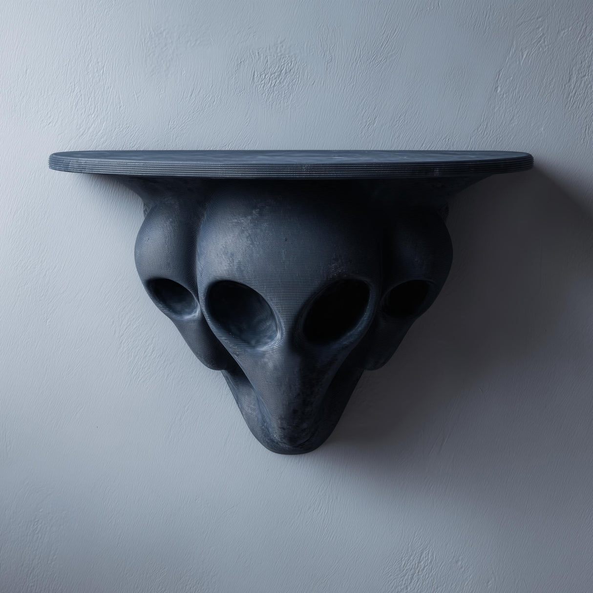 3D printed dark gray wall shelf with three elongated alien heads forming a sculptural support and a flat floating ledge on a light textured wall.
