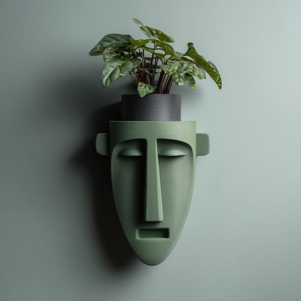 3D printed wall mounted face-shaped shelf sculpture in matte green PLA with minimalist facial features, displayed on a modern interior wall without a pot.