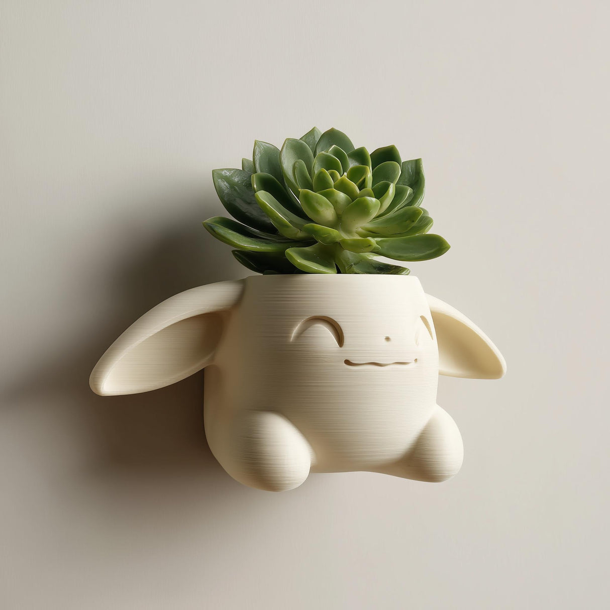 3D printed kawaii bunny wall planter in matte cream PLA mounted on a neutral wall, holding a small green succulent plant.