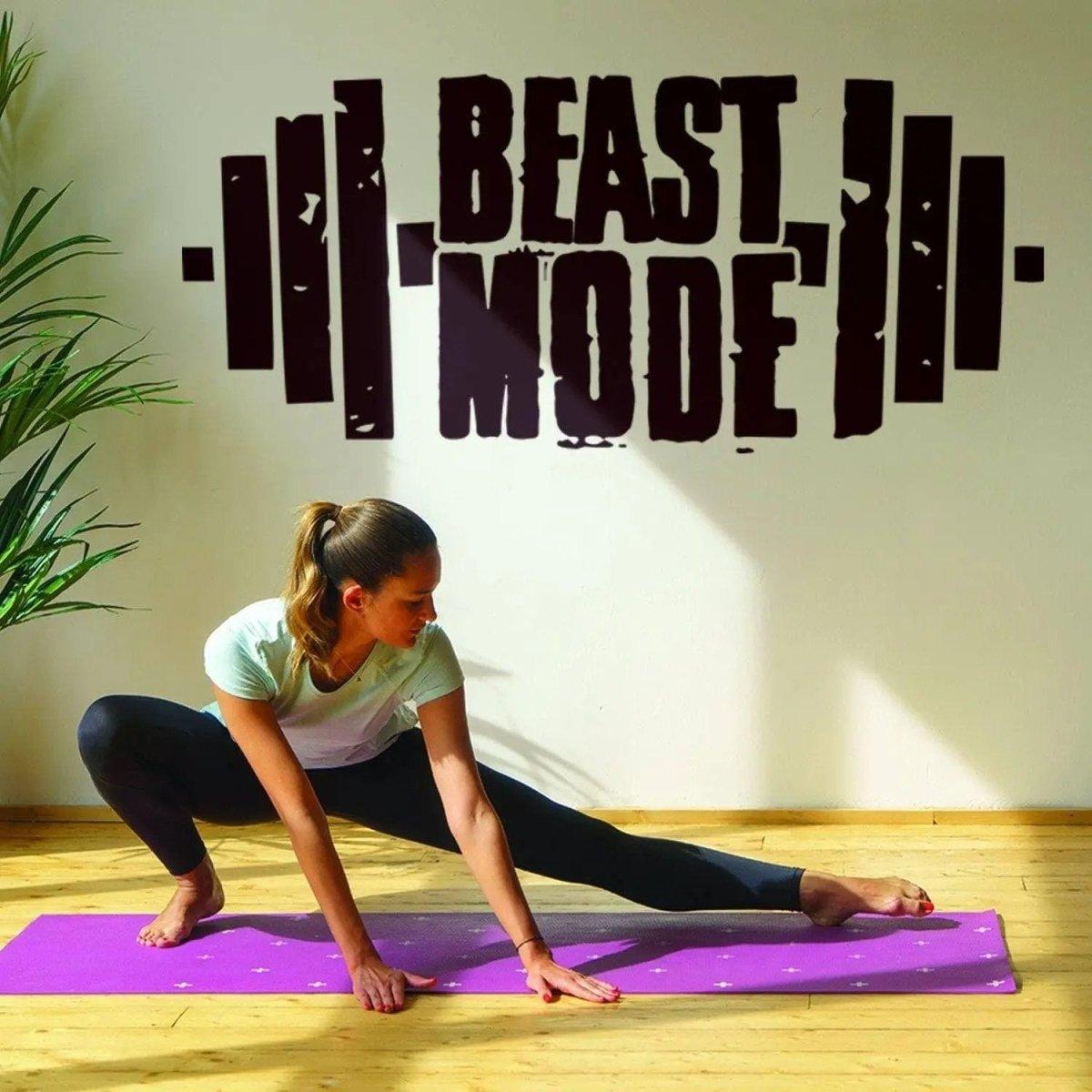 Woman stretching on a yoga mat with 'Beast Mode' motivational wall decal in background.