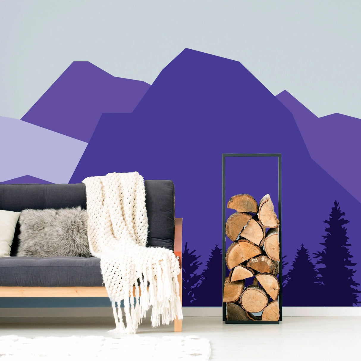 Majestic mountain wall decal in purple tones enhancing a cozy living room with a gray sofa and wood logs.
