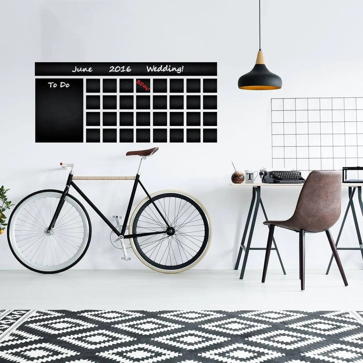 Large adhesive chalkboard monthly planner on wall, featuring workspace with bicycle and modern decor.