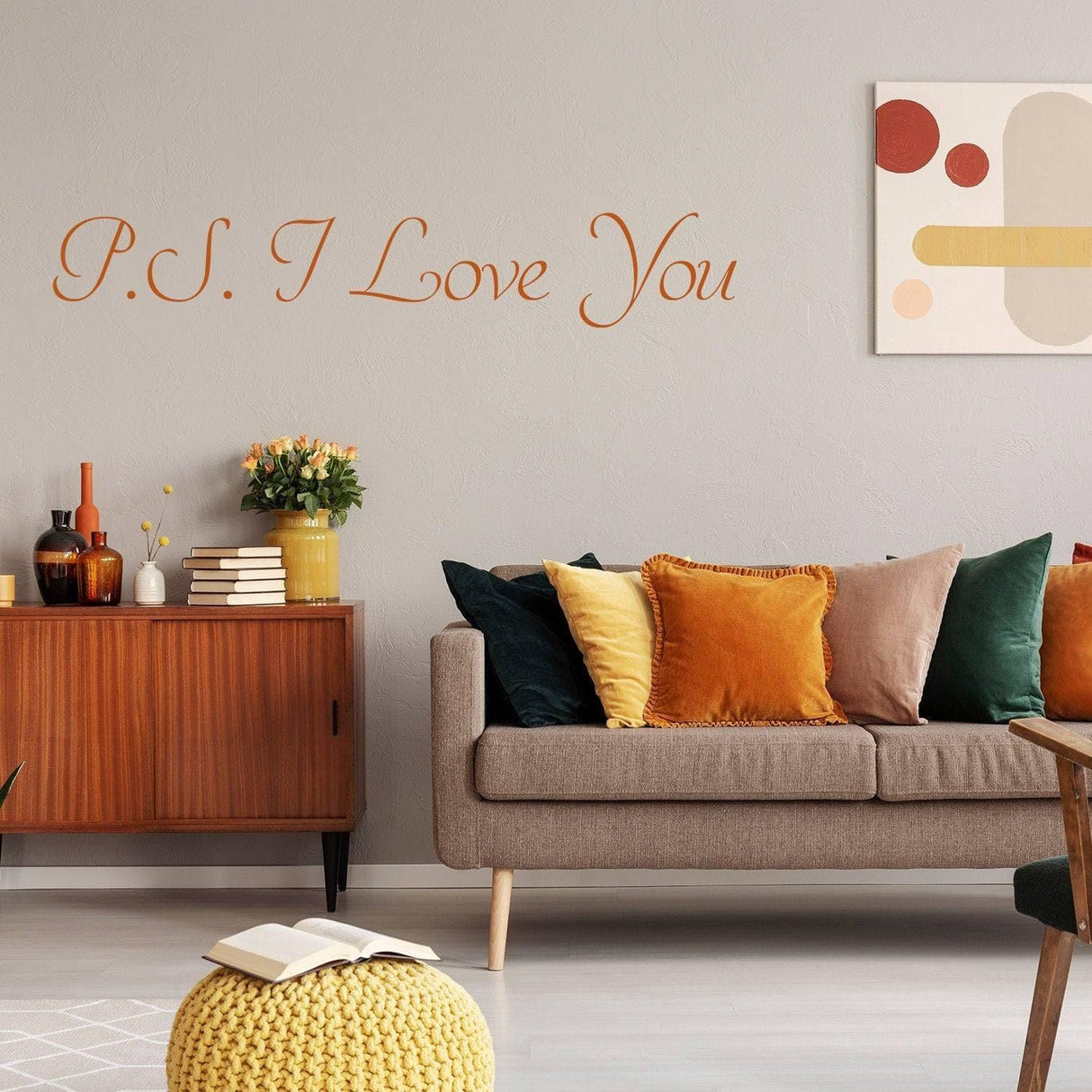 Romantic wall decal "P.S. I Love You" on a light gray wall above a stylish couch with colorful cushions.