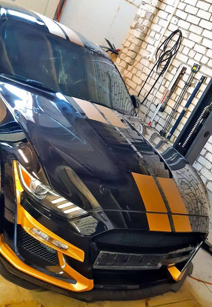 Sleek black car with orange racing stripes vinyl decals in garage, showcasing sporty vehicle graphics.