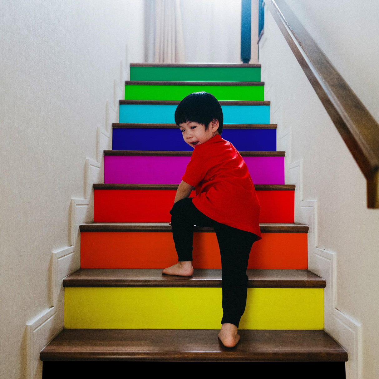 Child climbing colorful rainbow stair risers, vibrant decals brightening up the staircase.