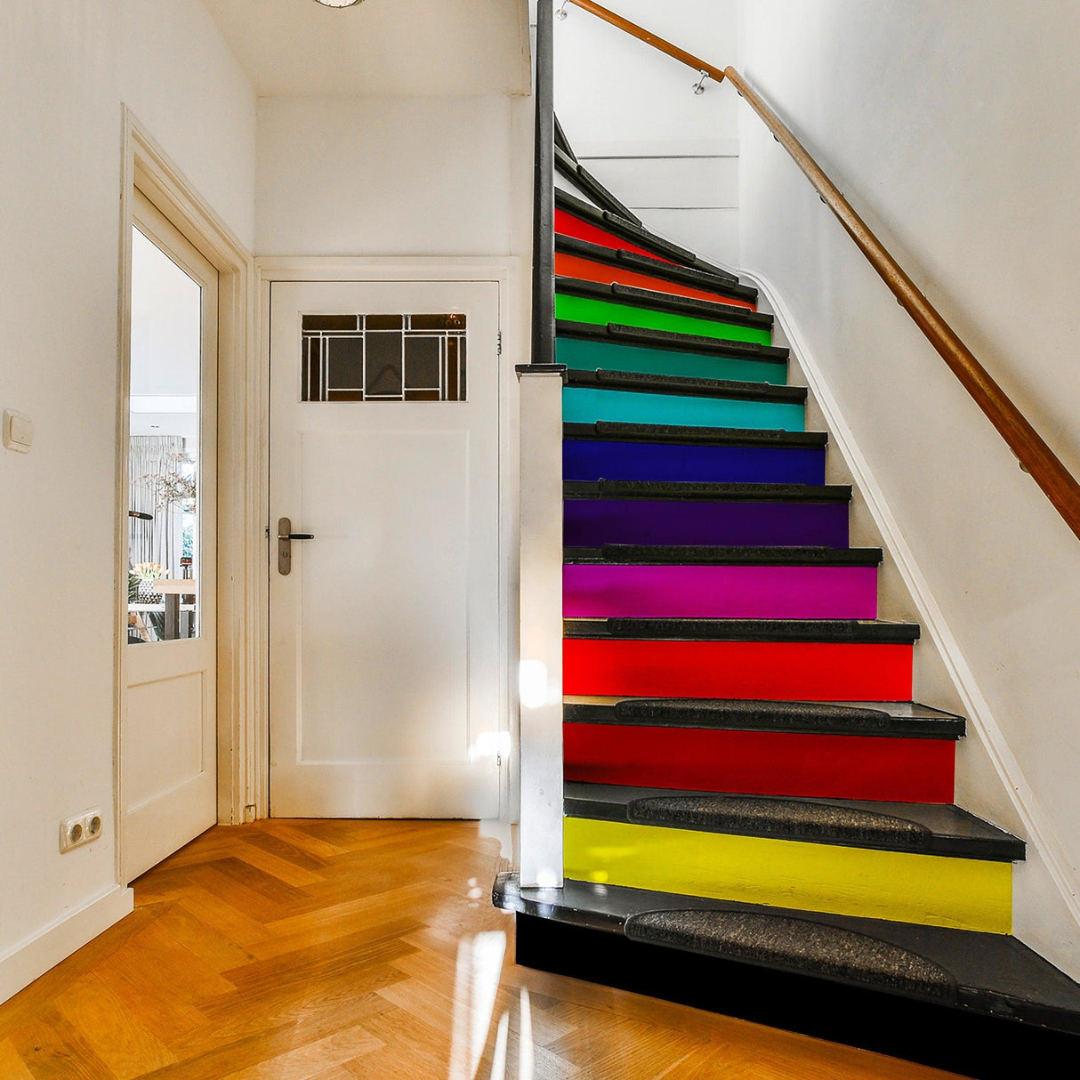 Vibrant rainbow stair riser decals transforming a staircase with colorful gradient steps in a bright hallway.