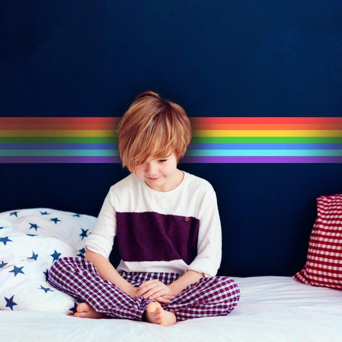 Child sitting on a bed with a rainbow stripe vinyl sticker on the wall, adding playful color to the room.