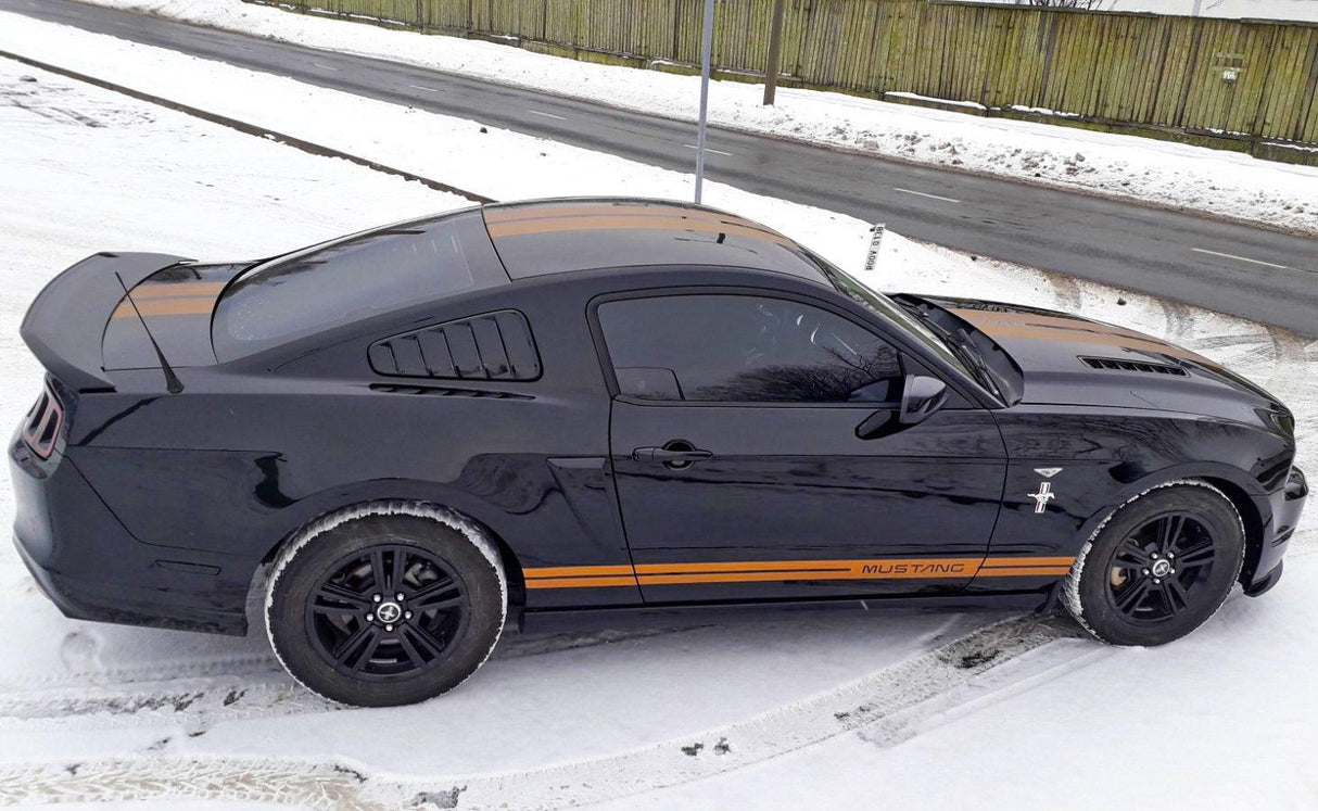 Black Mustang with orange racing stripes parked in snowy landscape showcasing stylish car decals.
