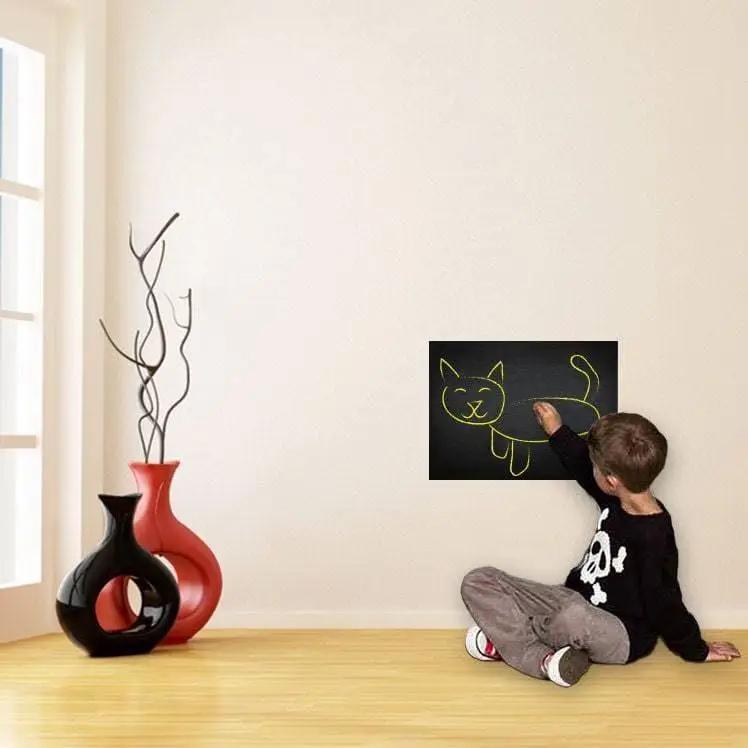 Child drawing a cat on a chalkboard wall sticker in a modern home setting.