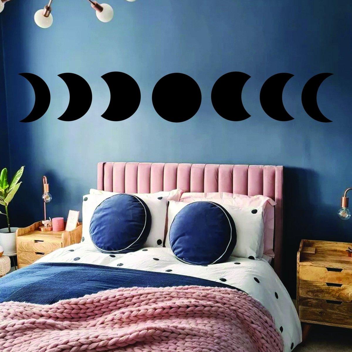 Moon phase wall decor stickers above a pink bed in a cozy bedroom setting with blue walls.