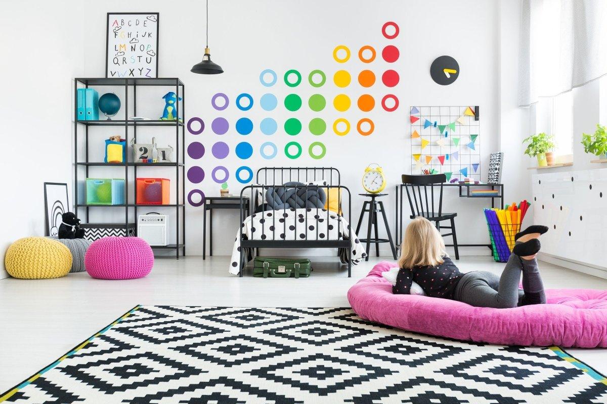 Colorful circle wall decals in a vibrant kids' room with a girl lounging on a pink cushion.