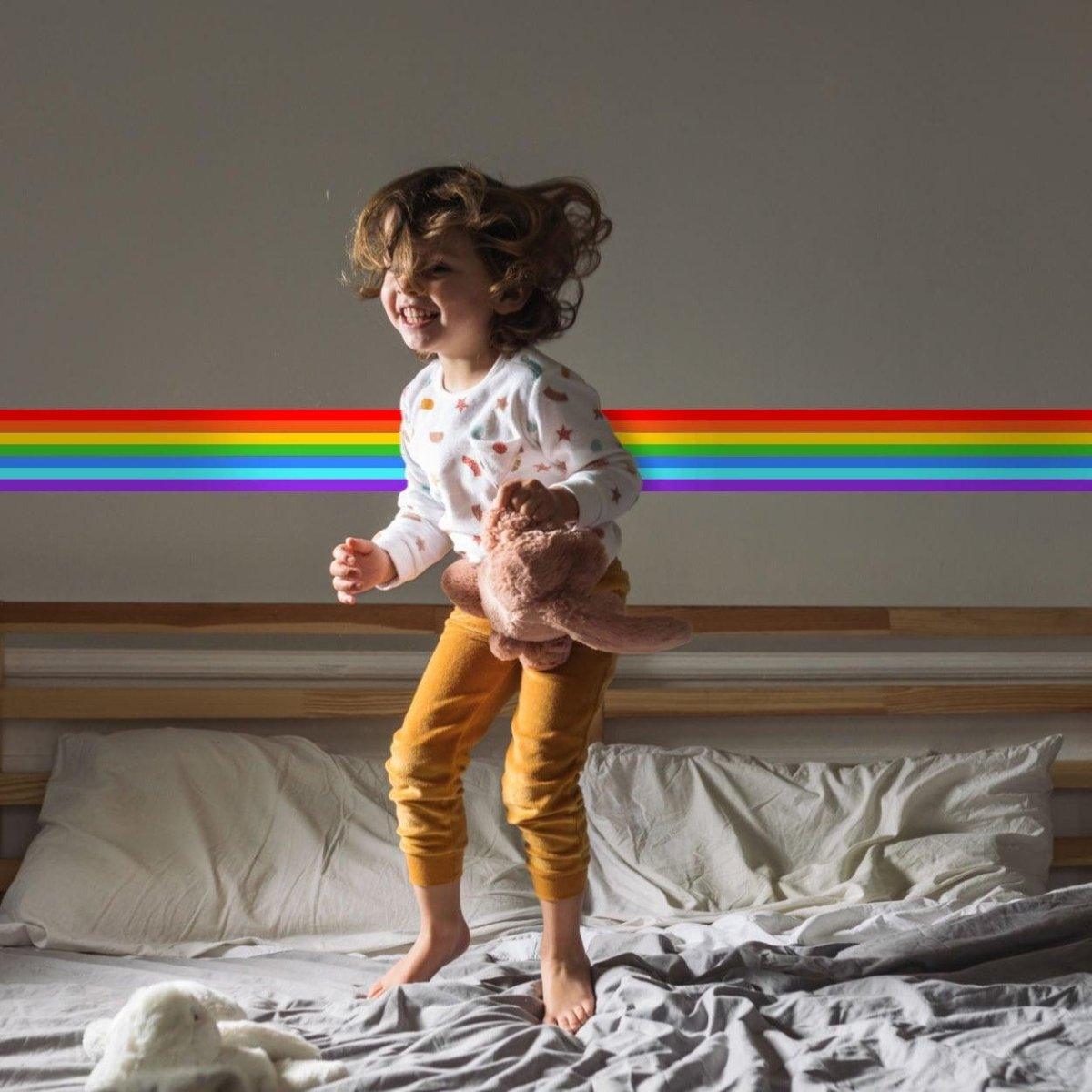 Child joyfully jumping on bed under a vibrant rainbow wall decal, showcasing a playful and colorful space.